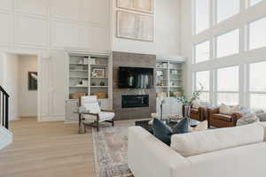 Living room featuring a towering ceiling, light wood-style flooring, a decorative wall, and a high end fireplace