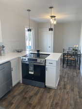 Kitchen featuring white cabinetry, light countertops, appliances with stainless steel finishes, dark wood-style floors, and decorative light fixtures