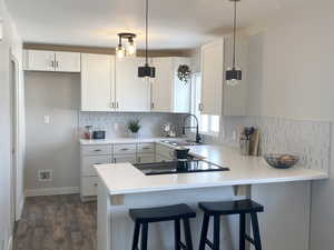 Kitchen with light countertops, a sink, white cabinets, and pendant lighting