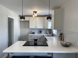 Kitchen featuring black electric cooktop, a sink, white cabinetry, light countertops, and decorative light fixtures