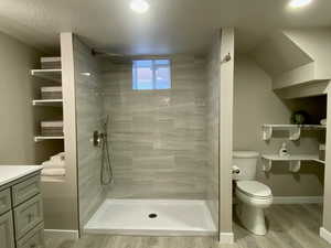 Bathroom featuring a walk in shower, toilet, wood finished floors, vanity, and baseboards