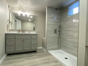 Full bathroom featuring walk in shower, vanity, baseboards, and wood finished floors