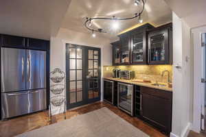 Bar featuring tasteful backsplash, wine cooler, freestanding refrigerator, wet bar, and a sink