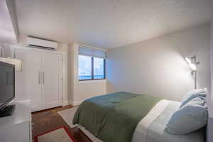 Bedroom featuring a textured ceiling, a wall mounted air conditioner, and baseboards