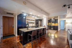 Kitchen with visible vents, decorative backsplash, glass insert cabinets, freestanding refrigerator, and a kitchen island with sink