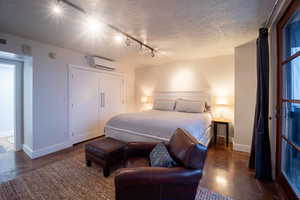 Bedroom with a textured ceiling, a wall unit AC, finished concrete floors, and baseboards