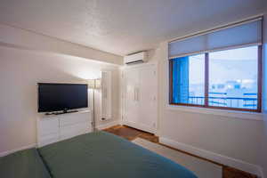 Unfurnished bedroom with a textured ceiling, an AC wall unit, and baseboards