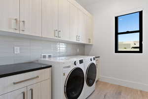 Washroom featuring light wood-style floors, cabinet space, washer and clothes dryer, and baseboards