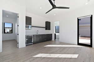 Interior space featuring light countertops, light wood-style flooring, backsplash, a sink, and beverage cooler