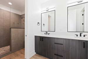 Bathroom featuring wood finished floors, double vanity, a sink, and walk in shower