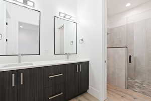 Bathroom featuring double vanity, wood finished floors, a sink, and a shower stall