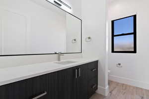 Bathroom featuring toilet, baseboards, wood finished floors, and vanity