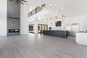 Unfurnished living room featuring a towering ceiling, a fireplace, light wood-style flooring, and a sink