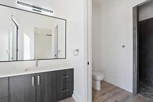 Bathroom with visible vents, toilet, vanity, wood finished floors, and baseboards