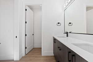 Full bathroom featuring wood finished floors, a sink, baseboards, and double vanity