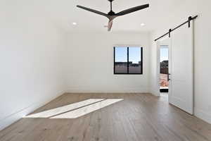 Empty room featuring a barn door, light wood-style flooring, a ceiling fan, and recessed lighting