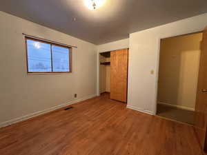 Unfurnished bedroom with baseboards, a closet, visible vents, and wood finished floors