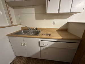 Kitchen featuring dark floors, white cabinets, a sink, and light countertops