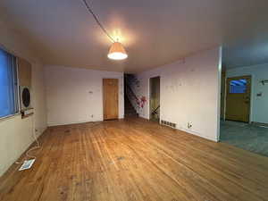 Empty room featuring stairs, stacked washer / dryer, wood finished floors, and visible vents