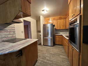 Kitchen with light countertops, appliances with stainless steel finishes, brown cabinets, tasteful backsplash, and a kitchen bar