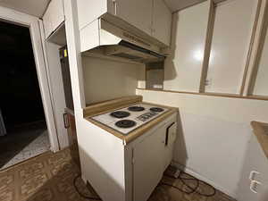 Kitchen featuring dark floors, under cabinet range hood, white cabinetry, light countertops, and white electric cooktop