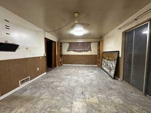 Spare room featuring a wainscoted wall, ceiling fan, wood walls, and visible vents