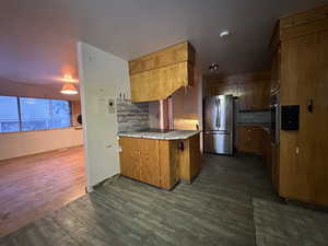 Kitchen featuring appliances with stainless steel finishes, light countertops, brown cabinetry, and dark wood-style floors