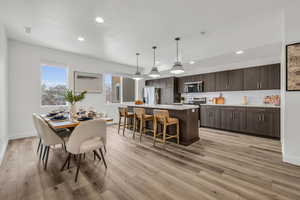 Interior space with pendant lighting, light countertops, stainless steel microwave, dark brown cabinets, and an island with sink