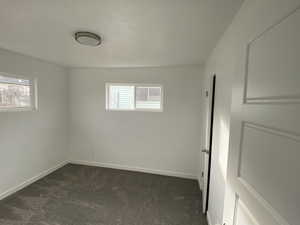 Unfurnished bedroom featuring dark colored carpet, multiple windows, and baseboards