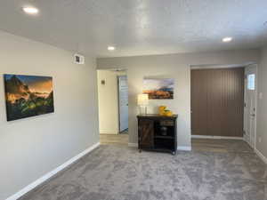 Carpeted foyer with a textured ceiling, recessed lighting, visible vents, and baseboards