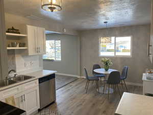 Kitchen with a sink, white cabinetry, hanging light fixtures, stainless steel dishwasher, and light countertops