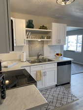 Kitchen with open shelves, white cabinets, dishwasher, and light countertops