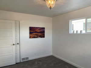 Spare room with visible vents, dark carpet, a textured ceiling, and baseboards