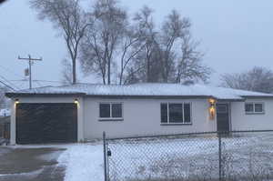 View of snow covered exterior featuring a garage, driveway, a shingled roof, fence, and brick siding