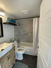 Bathroom with toilet, a textured ceiling, shower / bath combination with curtain, and vanity