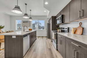 Kitchen featuring a center island with sink, a breakfast bar area, stainless steel appliances, hanging light fixtures, and a sink