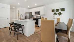 Kitchen with a kitchen island with sink, a sink, light countertops, appliances with stainless steel finishes, and a kitchen bar