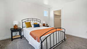 Bedroom with dark colored carpet, a walk in closet, and baseboards