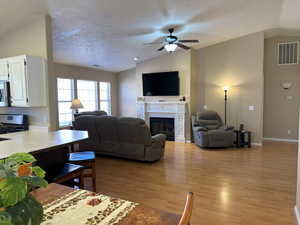 Living room featuring light wood finished floors, visible vents, vaulted ceiling, a textured ceiling, and a fireplace