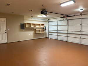 Garage featuring visible vents, electric panel, and a garage door opener