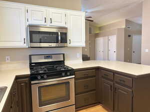 Kitchen featuring appliances with stainless steel finishes, light countertops, white cabinets, and a peninsula