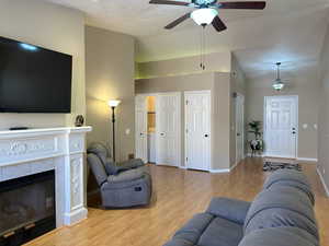 Living area featuring lofted ceiling, light wood-style flooring, a ceiling fan, a tile fireplace, and baseboards