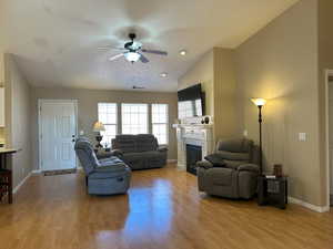 Living area featuring light wood finished floors, ceiling fan, a fireplace, and baseboards