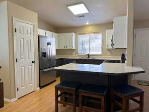 Kitchen with appliances with stainless steel finishes, a breakfast bar area, visible vents, and white cabinets