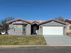 View of front of house featuring concrete driveway, a tile roof, a front lawn, and stucco siding