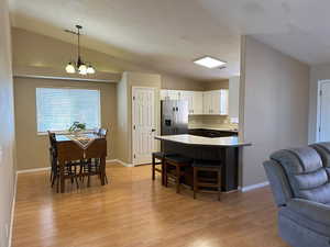 Interior space with white cabinets, vaulted ceiling, stainless steel refrigerator with ice dispenser, a kitchen bar, and decorative light fixtures