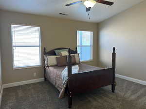 Bedroom featuring ceiling fan, dark colored carpet, visible vents, and baseboards