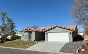 View of front facade featuring an attached garage, a tile roof, concrete driveway, and stucco siding