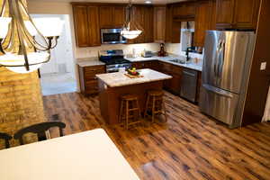 Kitchen featuring decorative light fixtures, a kitchen island, light stone countertops, sink, and appliances with stainless steel finishes