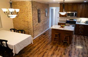 Kitchen with stainless steel appliances, hanging light fixtures, a kitchen island, light stone counters, and dark hardwood / wood-style floors